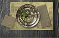 La Chinoiserie Fawn Party Table — plates stacked on the garden-scene placemat with fretwork napkins, in cream on umber, on dark wood