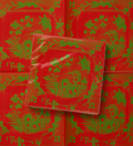 La Chinoiserie Noël dinner napkin folded over the open pattern — green garden scene on lacquer red