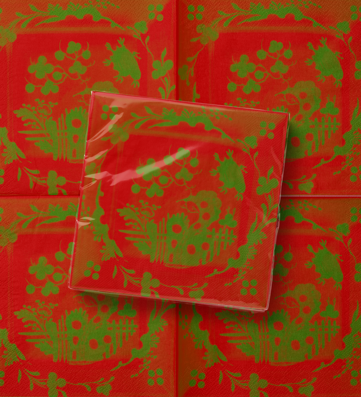 La Chinoiserie Noël dinner napkin folded over the open pattern — green garden scene on lacquer red