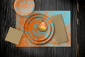 La Chinoiserie Orange Party Table — plates stacked on the garden-scene placemat with fretwork napkins, in aqua on orange, on dark wood