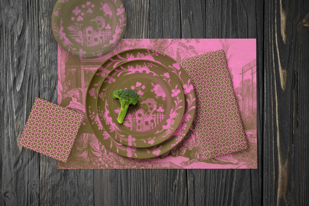 La Chinoiserie Pink Party Table — plates stacked on the garden-scene placemat with fretwork napkins, in rose on olive, on dark wood