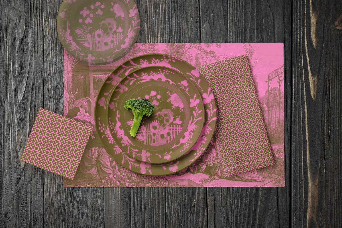 La Chinoiserie Pink Party Table — plates stacked on the garden-scene placemat with fretwork napkins, in rose on olive, on dark wood