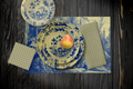 La Chinoiserie Porcelain Party Table — plates stacked on the garden-scene placemat with fretwork napkins, in blue on ivory, on dark wood
