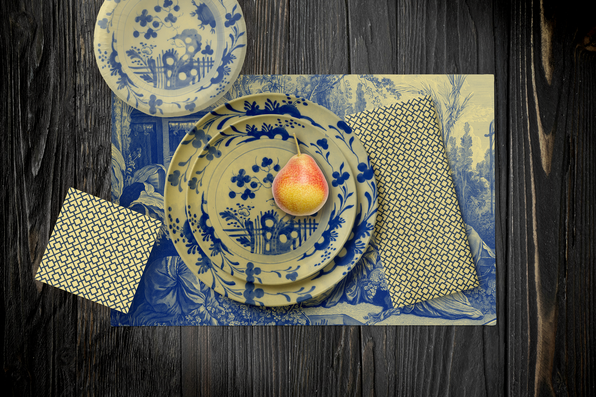 La Chinoiserie Porcelain Party Table — plates stacked on the garden-scene placemat with fretwork napkins, in blue on ivory, on dark wood