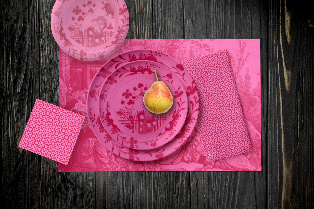 La Chinoiserie Rouge Party Table — plates stacked on the garden-scene placemat with fretwork napkins, in red on pink, on dark wood
