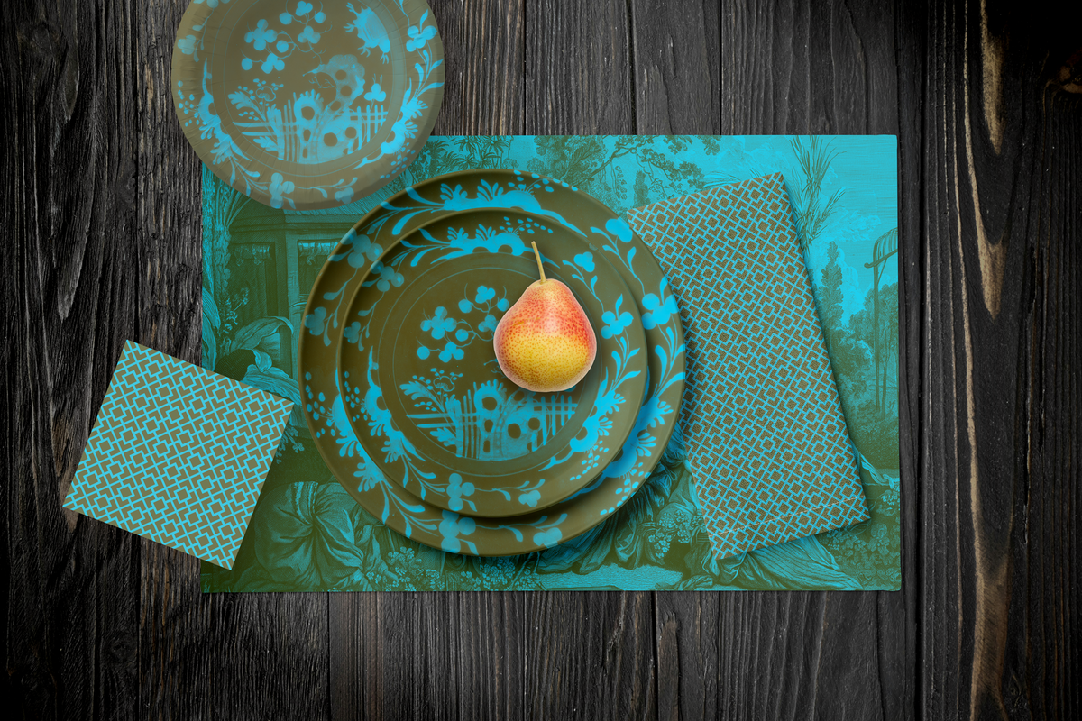 La Chinoiserie Teal Party Table — plates stacked on the garden-scene placemat with fretwork napkins, in teal on olive, on dark wood