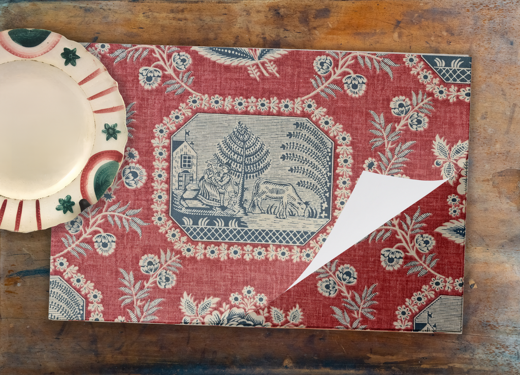 Decorative red placemat with floral and landscape design on a wooden surface