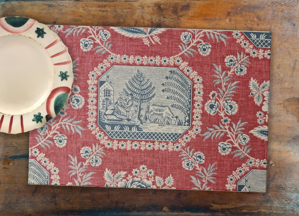 Decorative red placemat with floral and landscape design on a wooden surface