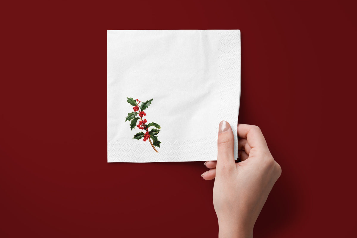 Noël Holly paper napkins on a deep red ground — a napkin held in hand