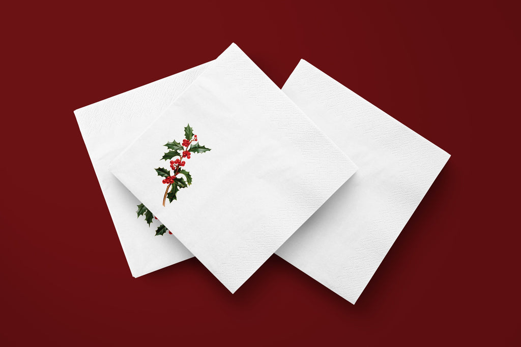 Noël Holly paper napkins on a deep red ground — three napkins scattered