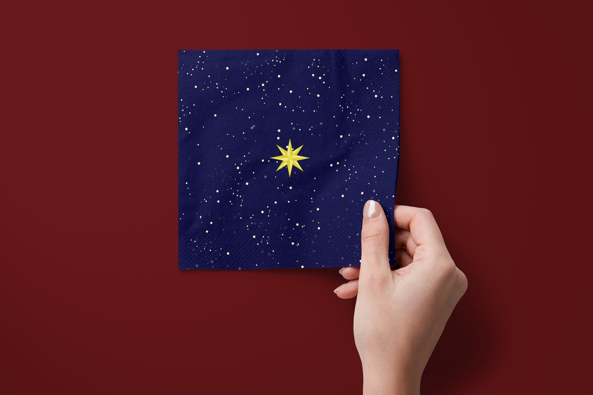 Noël La Nuit Étoilée paper napkins on a deep red ground — a napkin held in hand
