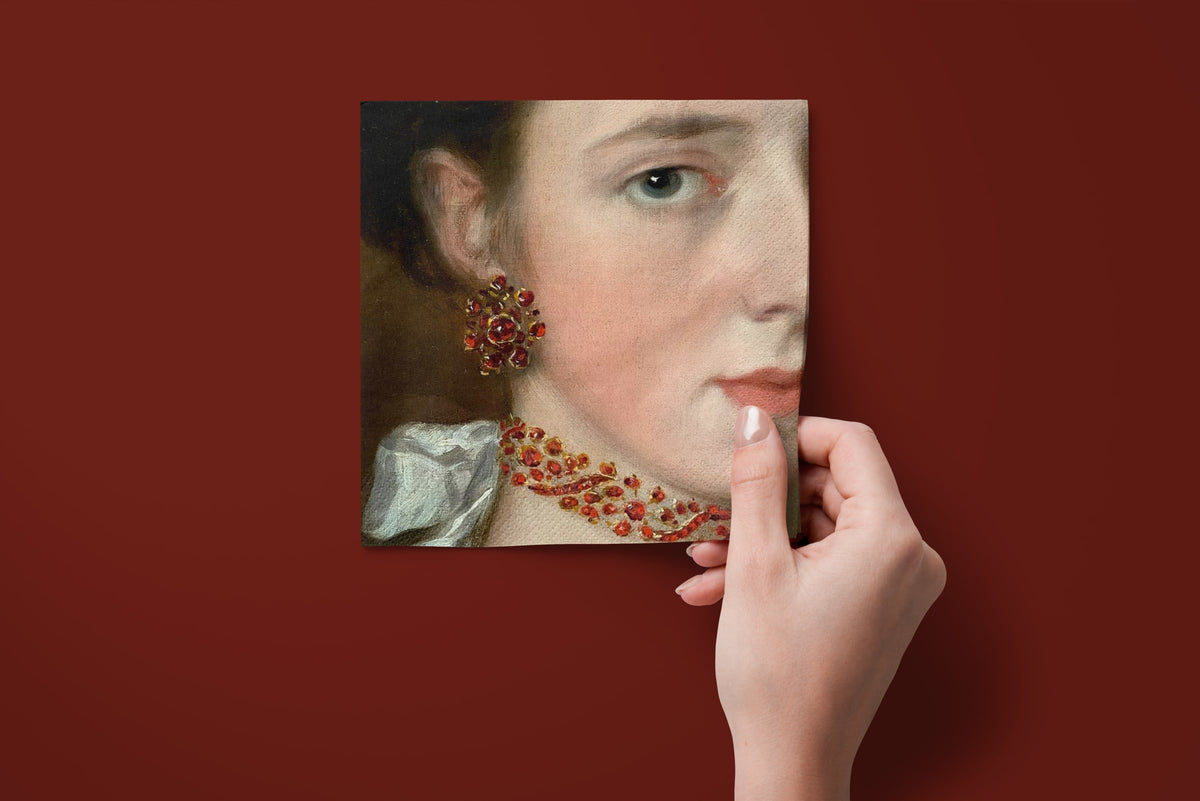 Noël La Parure paper napkins on a deep red ground — a napkin held in hand