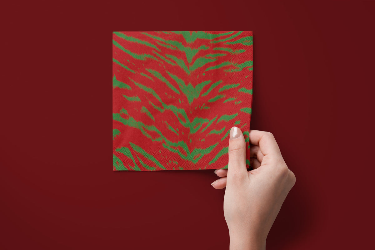 Noël Le Tigre paper napkins on a deep red ground — a napkin held in hand