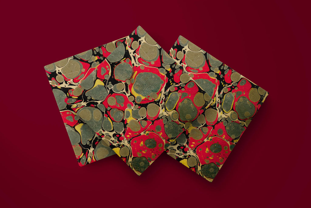 Noël Marbré Rouge paper napkins on a deep red ground — three napkins scattered