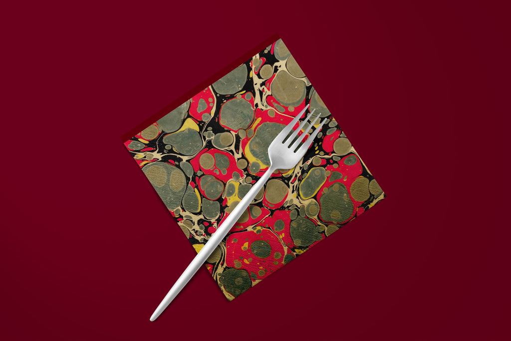 Noël Marbré Rouge paper napkins on a deep red ground — a napkin with a fork