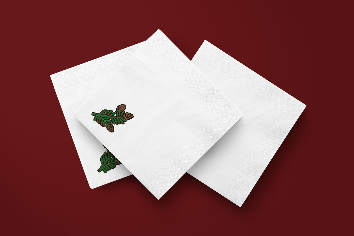 Noël Mini Pinecone paper napkins on a deep red ground — three napkins scattered