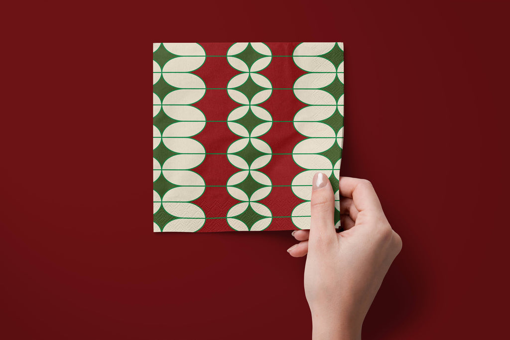 Noël Mod paper napkins on a deep red ground — a napkin held in hand