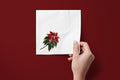 Noël Poinsettia paper napkins on a deep red ground — a napkin held in hand