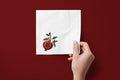 Noël Pomegranate paper napkins on a deep red ground — a napkin held in hand