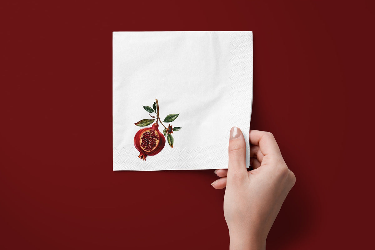 Noël Pomegranate paper napkins on a deep red ground — a napkin held in hand