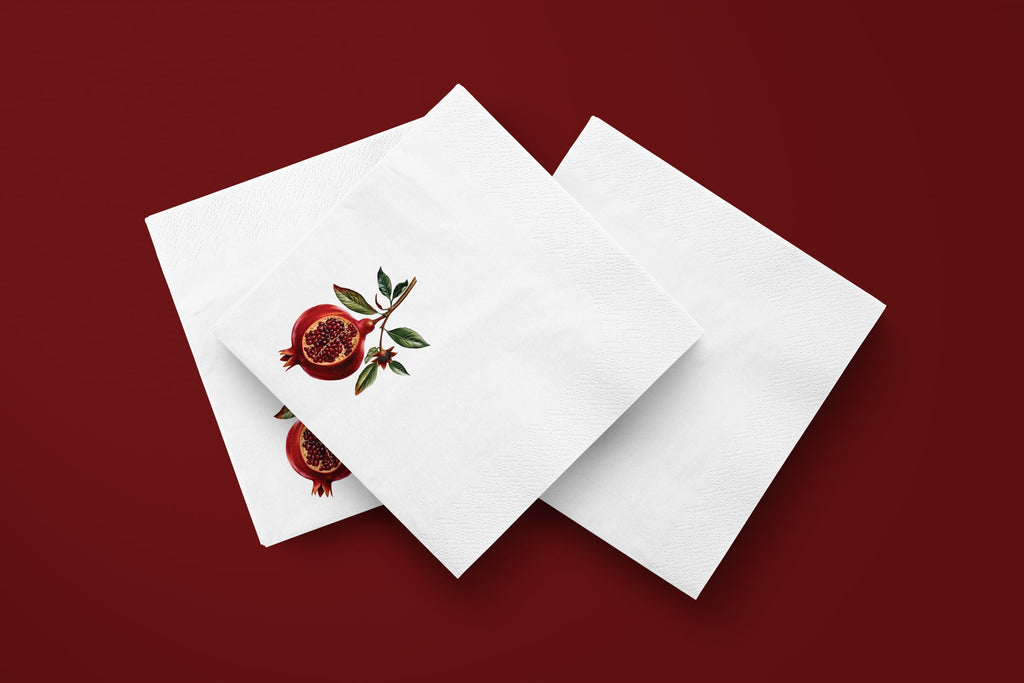 Noël Pomegranate paper napkins on a deep red ground — three napkins scattered