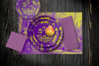La Chinoiserie Violet Party Table — plates stacked on the garden-scene placemat with fretwork napkins, in chartreuse on magenta, on dark wood