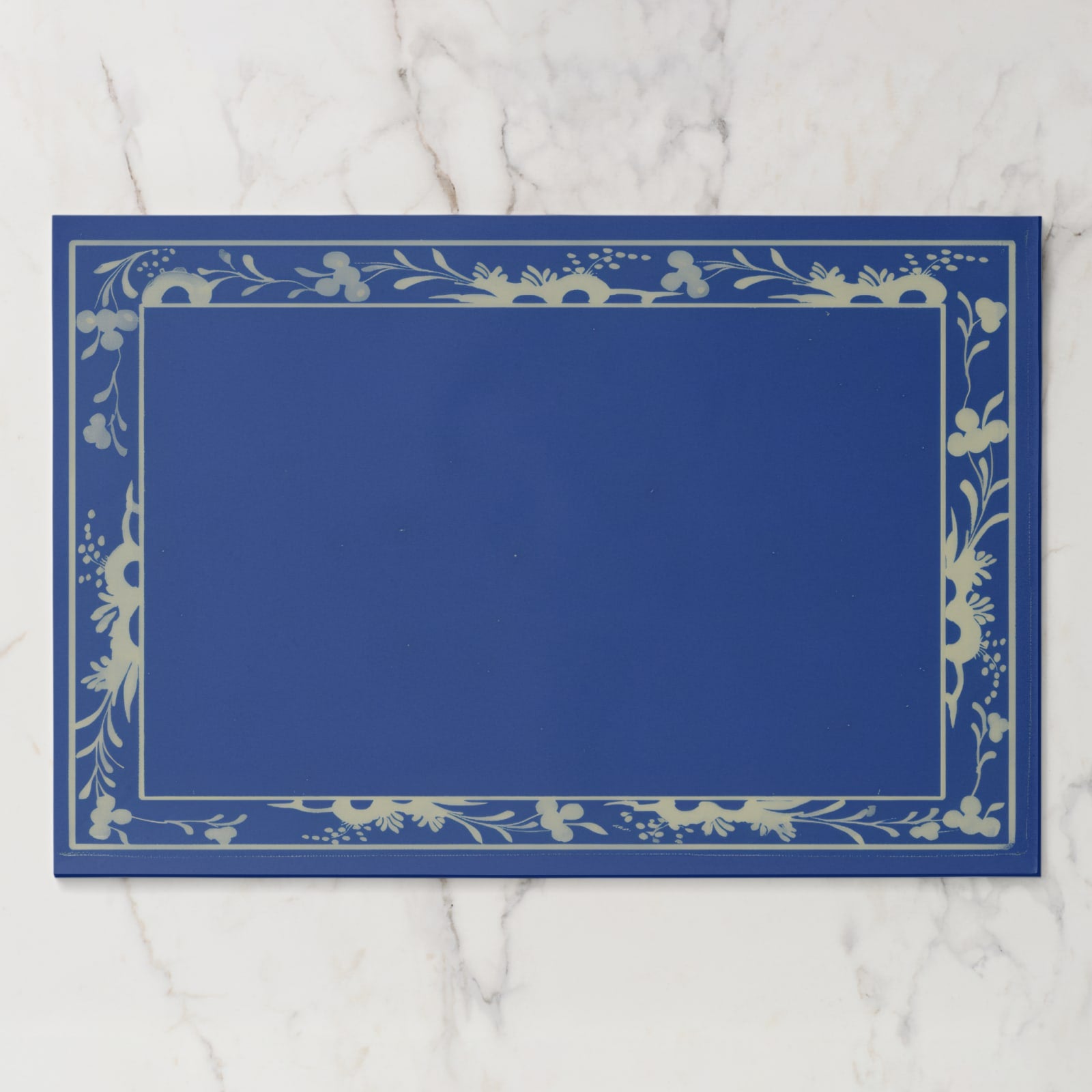 La Chinoiserie Bordure paper placemat in Cobalt — cream engraved floral border on cobalt blue, open centre