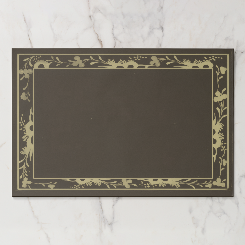 La Chinoiserie Bordure paper placemat in fawn — parchment engraved floral border on a deep umber ground