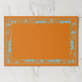 La Chinoiserie Bordure paper placemat in orange — pale blue engraved floral border on a tangerine ground