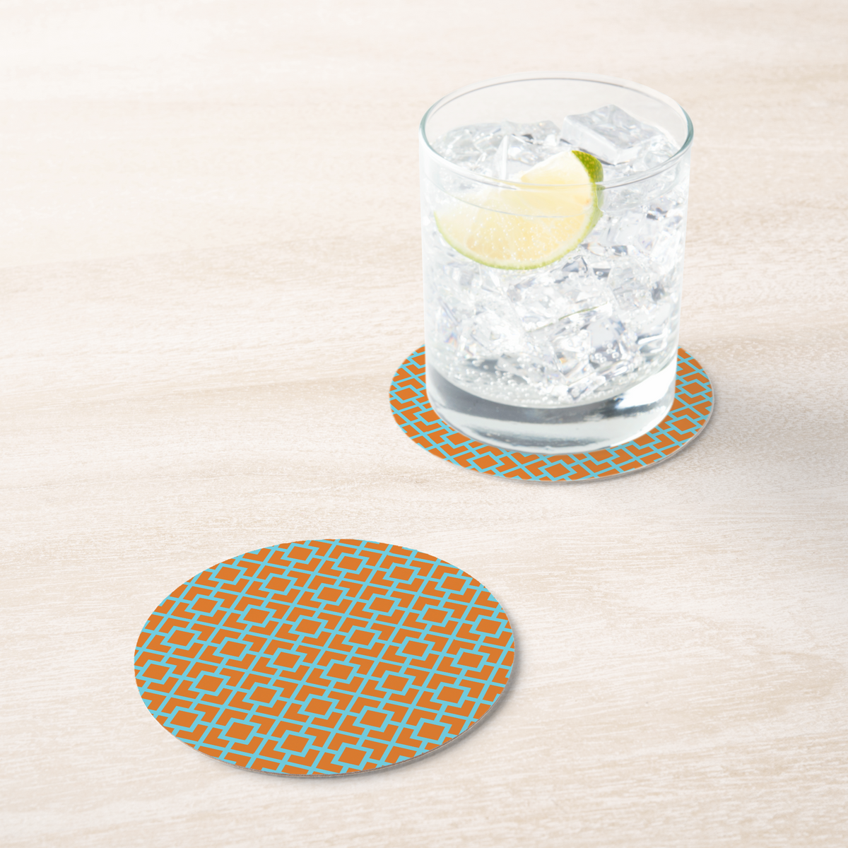 La Chinoiserie Orange Fretwork paper coaster under an iced drink on pale wood