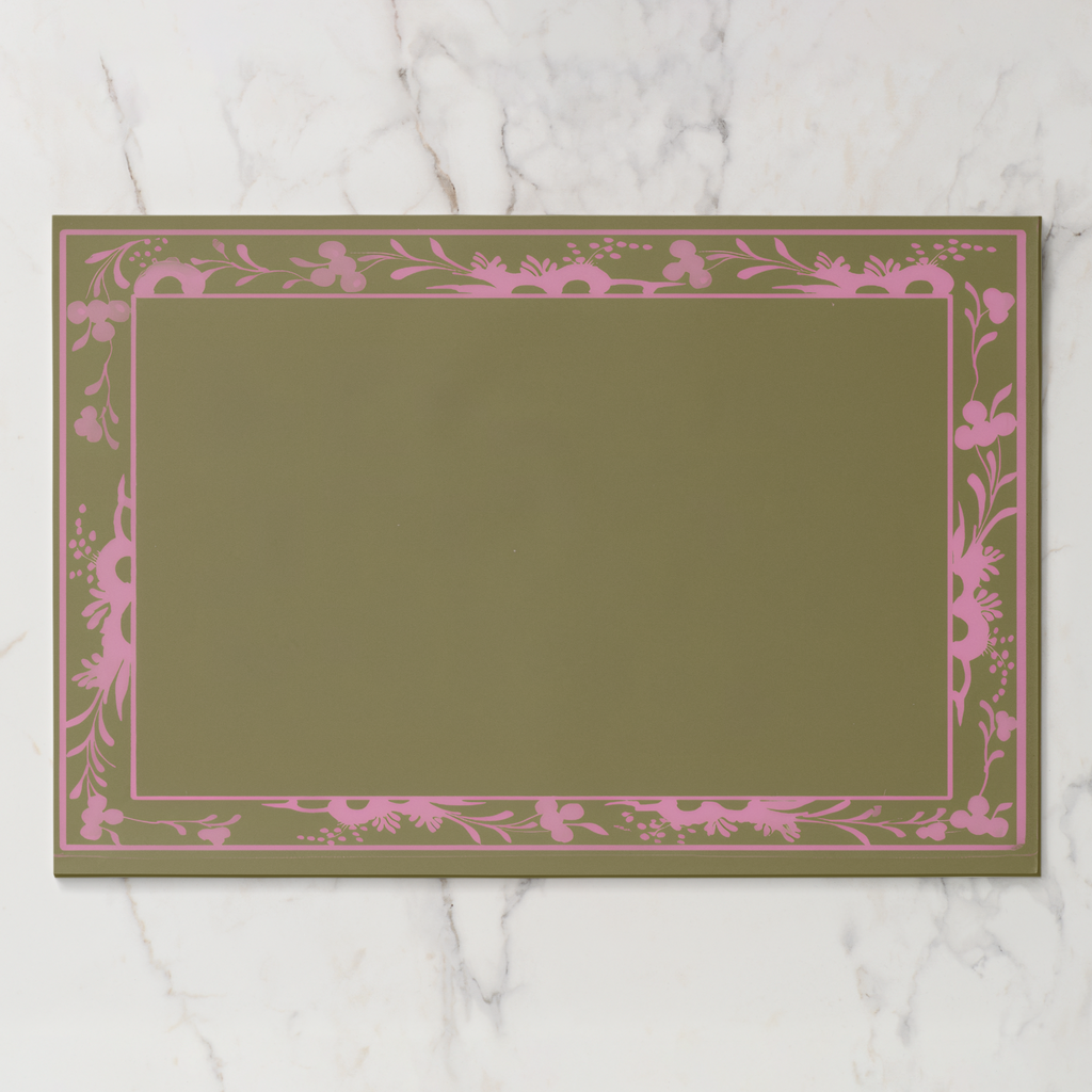 La Chinoiserie Bordure paper placemat in pink — pink engraved floral border on an olive ground