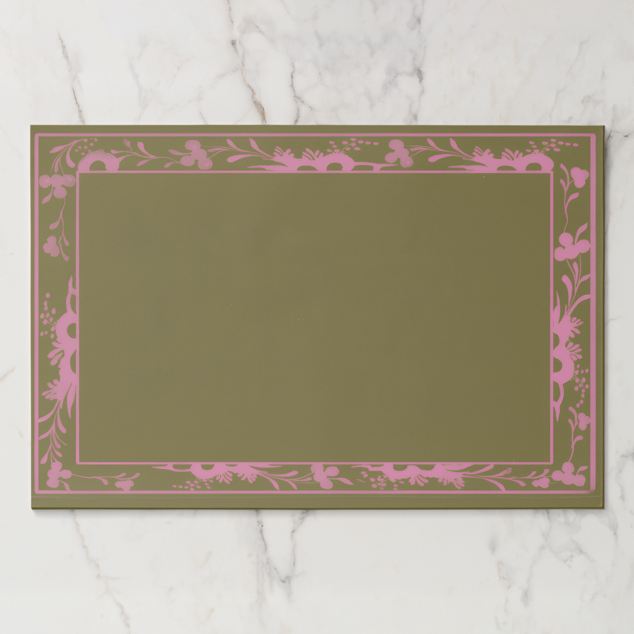 La Chinoiserie Bordure paper placemat in pink — pink engraved floral border on an olive ground