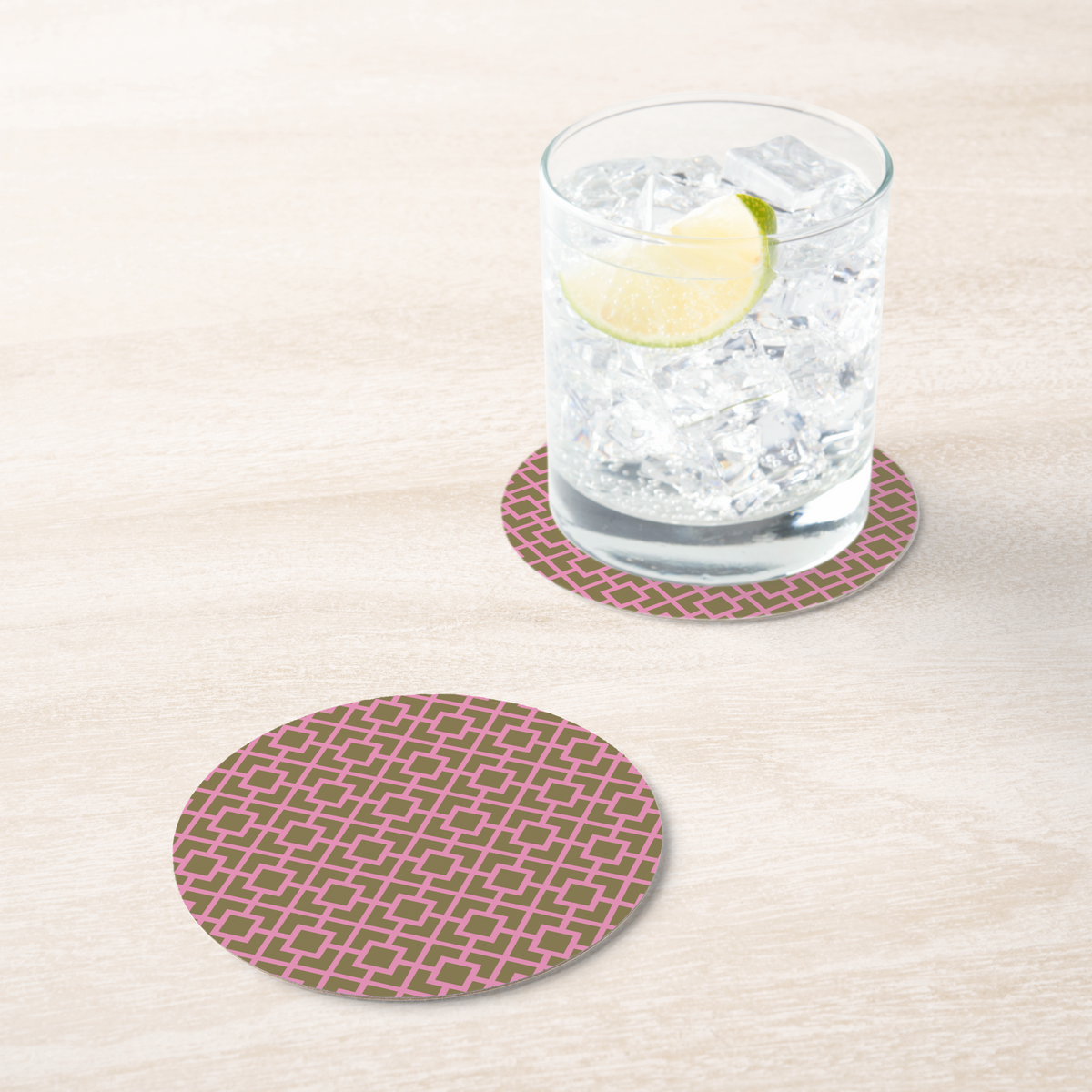 La Chinoiserie Pink Fretwork paper coaster under an iced drink on pale wood