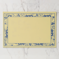 La Chinoiserie Bordure paper placemat in porcelain — navy engraved floral border on a butter-cream ground