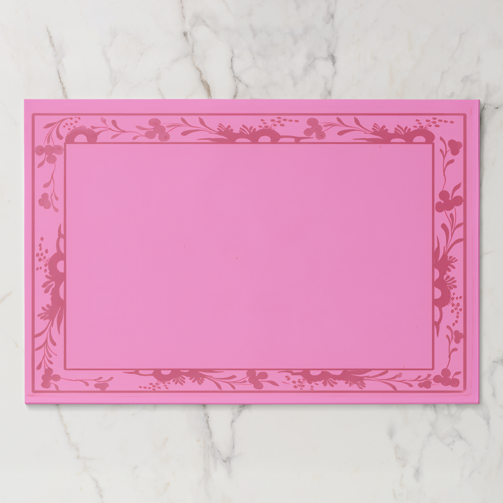 La Chinoiserie Bordure paper placemat in rouge — deep rose engraved floral border on a bright rose ground
