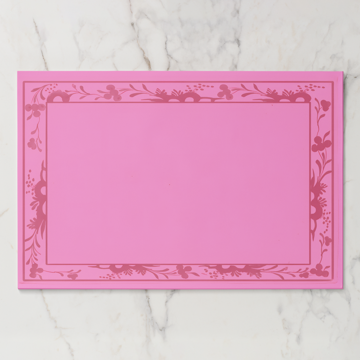 La Chinoiserie Bordure paper placemat in rouge — deep rose engraved floral border on a bright rose ground
