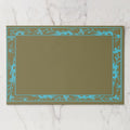 La Chinoiserie Bordure paper placemat in Teal — teal engraved floral border on olive, open centre