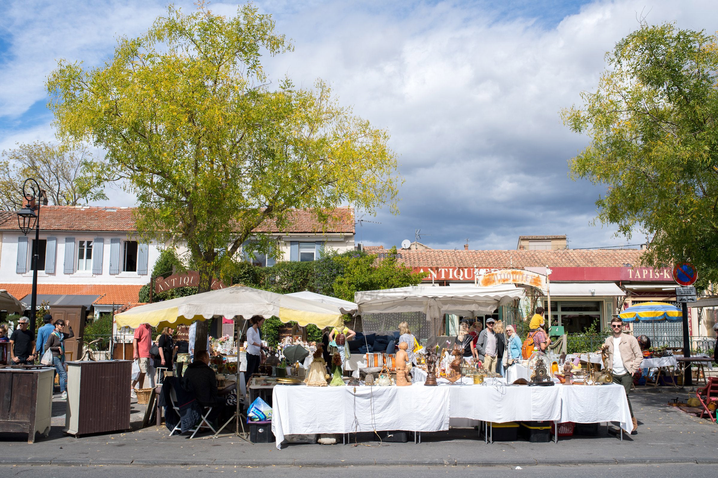 Outdoor market scene with stalls and people under a cloudy sky.